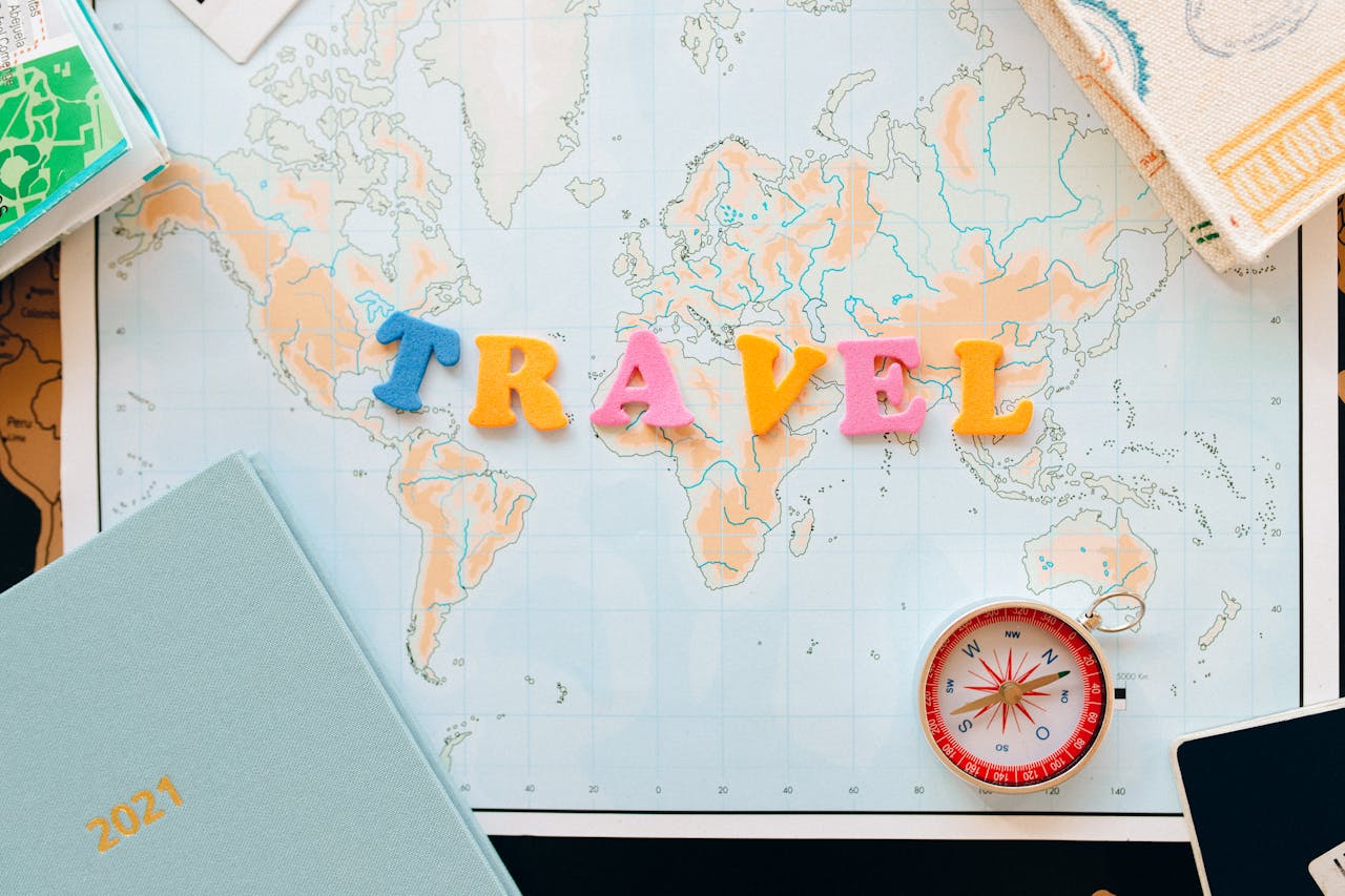 Flat lay of a map with colorful letters u0022TRAVELu0022 and a compass for planning adventures.