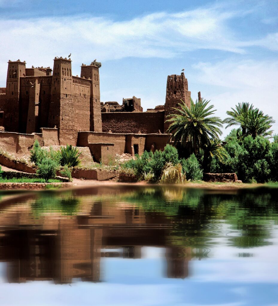 A scenic view of the ancient clay Kasbah Ait Benhaddou by the river in Morocco, under a clear blue sky.