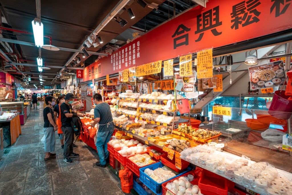 Colorful indoor market with people shopping at an Asian food stall.