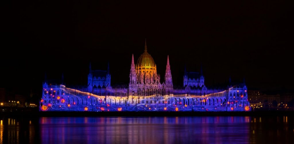 Vivid night view of Hungarian Parliament Building with colorful light projections.